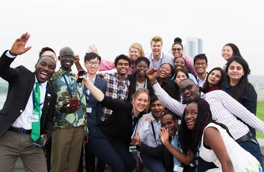 20 university students from across the Commonwealth smile and cheer together for a group photo in a park